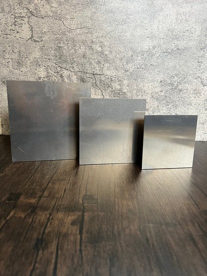 three various sized square aluminum blank metal pieces on a wood and concrete background