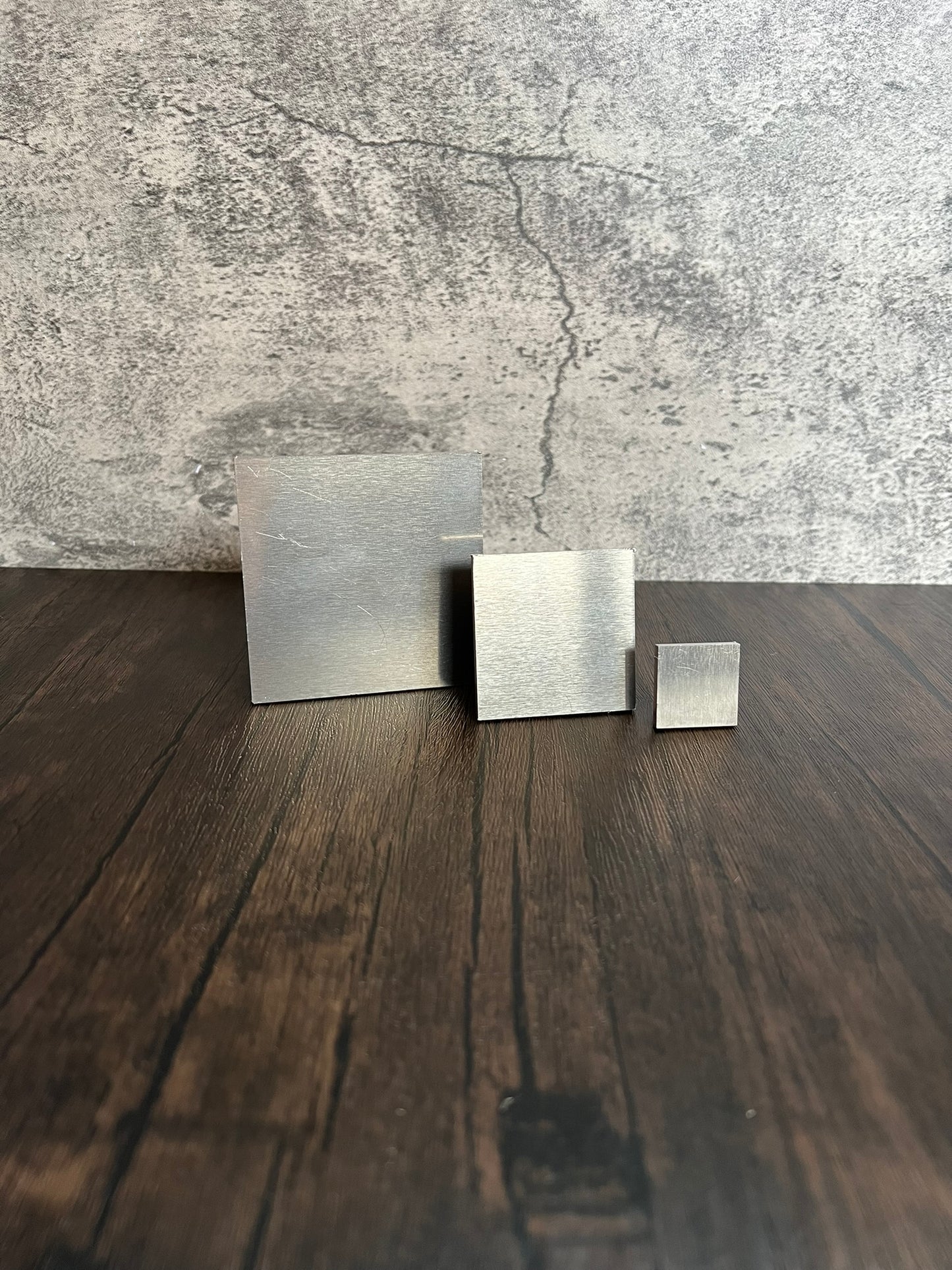 three various sized square aluminum blank metal pieces on a wood and concrete background